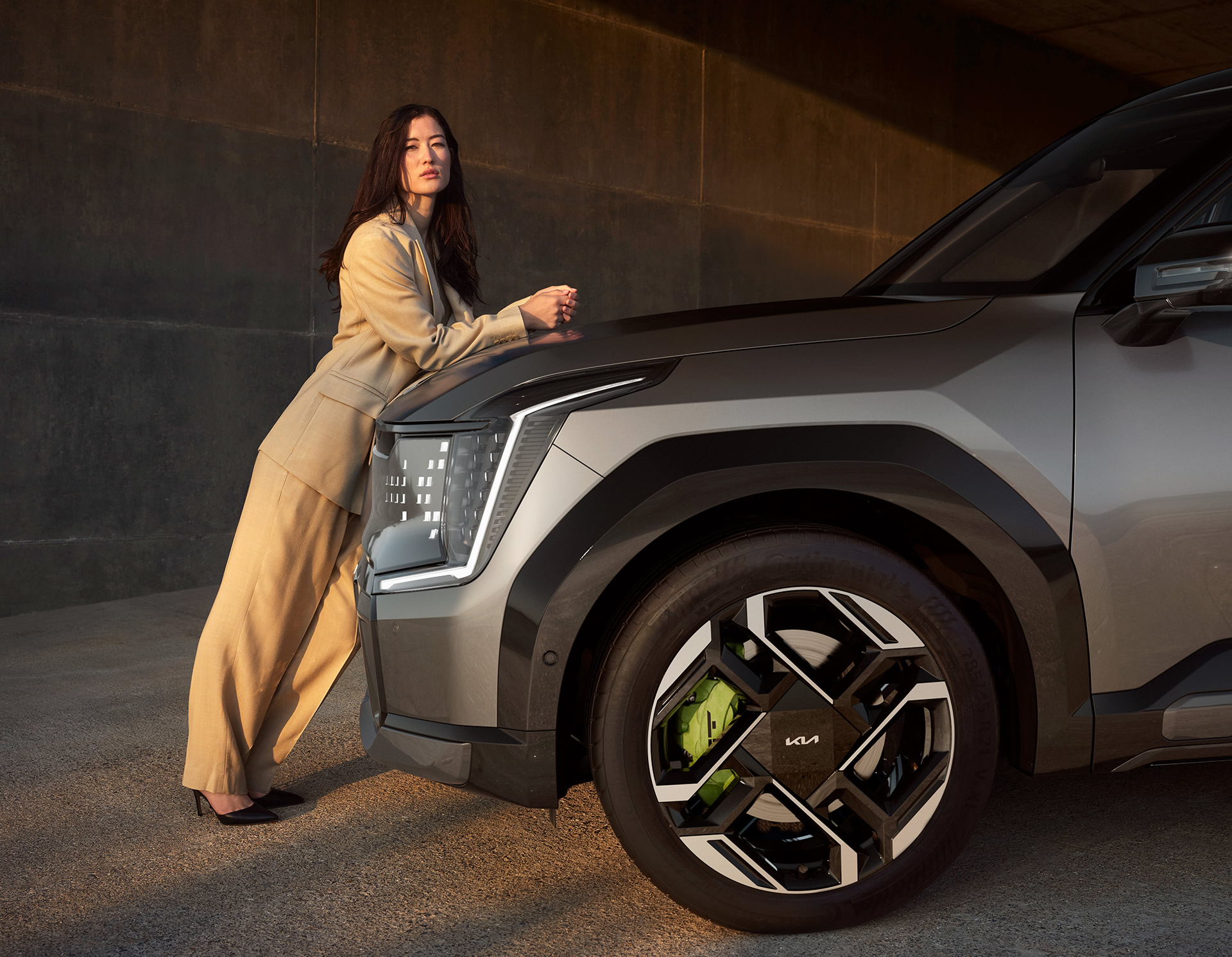 Kia EV9 GT, grau, Motorhaube Fahrerseite, Frau lehnt vorne am Fahrzeug